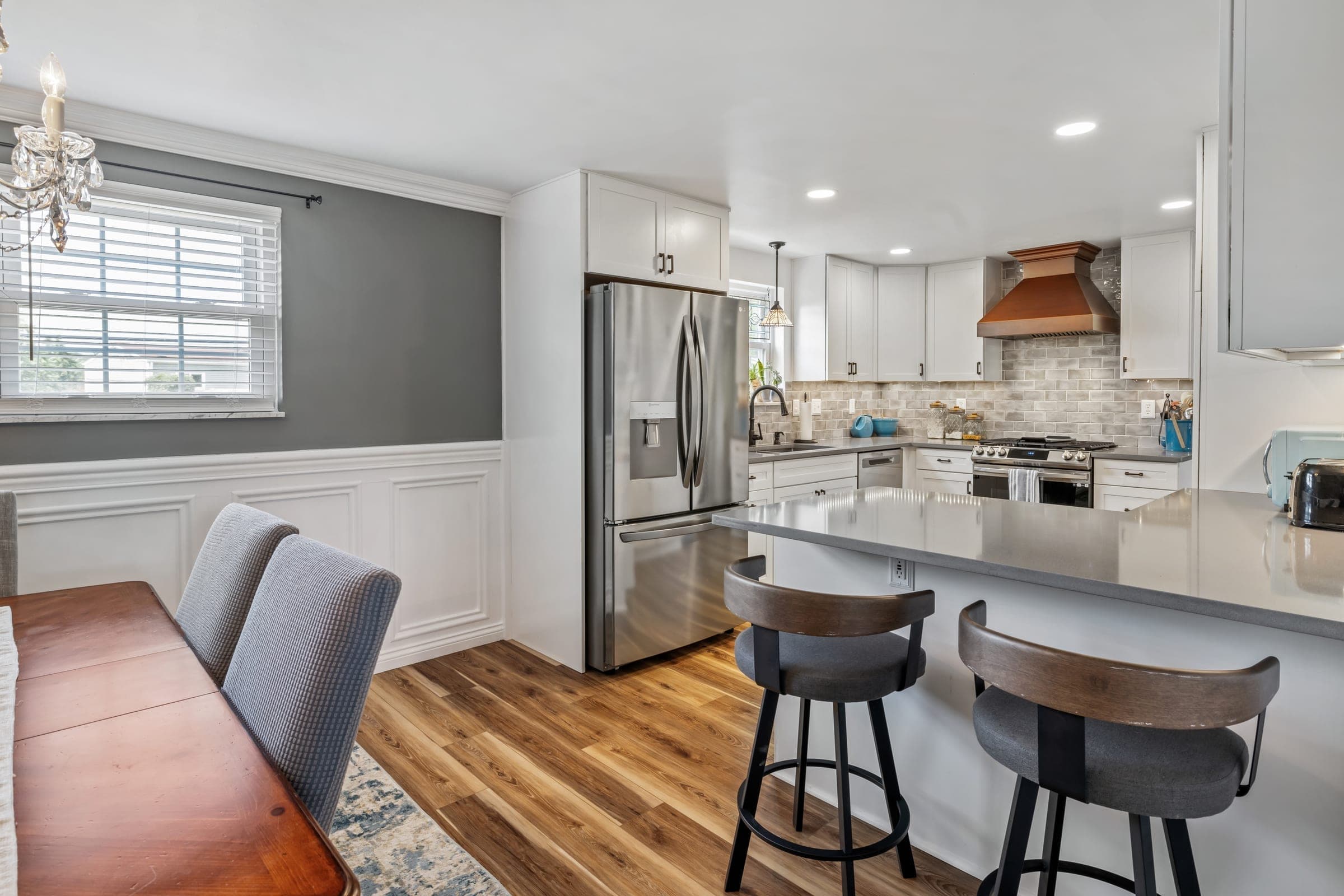 Open kitchen with a gray quartz peninsula, copper range hood, and adjoining dining area on Nix Drive in Whitehall, PA, built by Integrated Contracting & Renovations